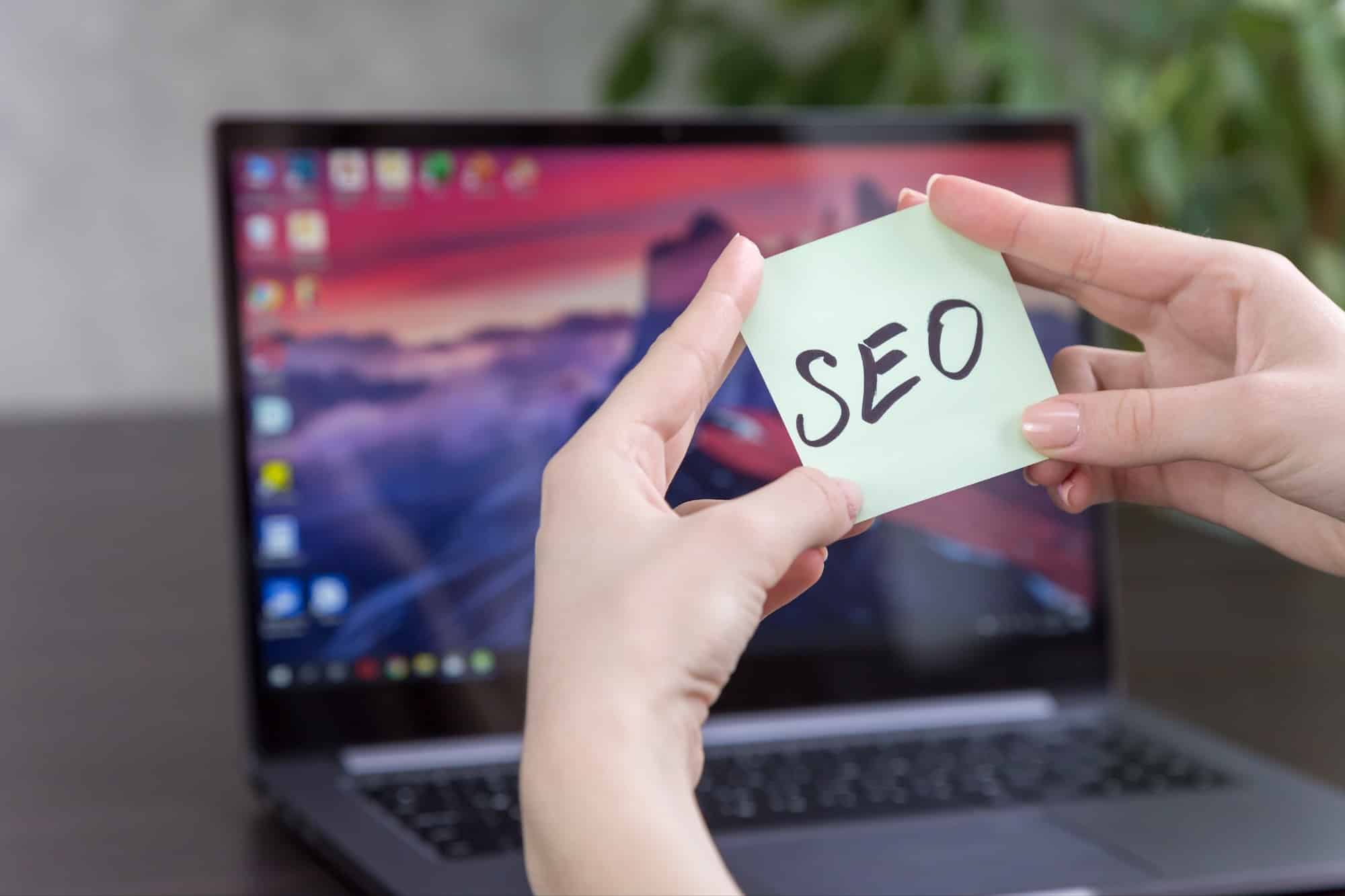 sticker with the inscription SEO in female hands on the background of a laptop sticker with the inscription SEO in female hands on the background of a laptop
